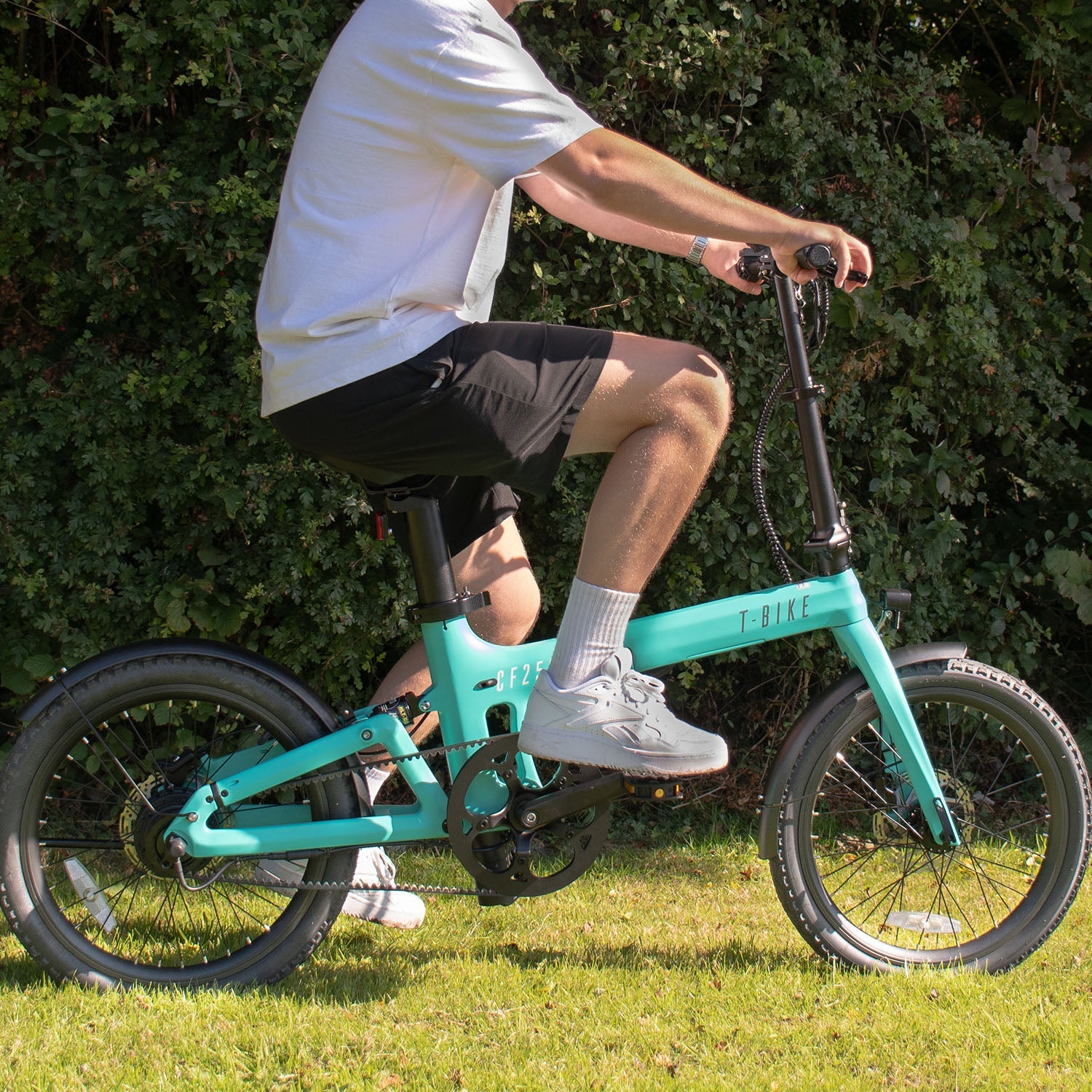 Image of a man riding Turquoise Carbon Fibre 250 folding E-Bike on grassy terrain in the sun