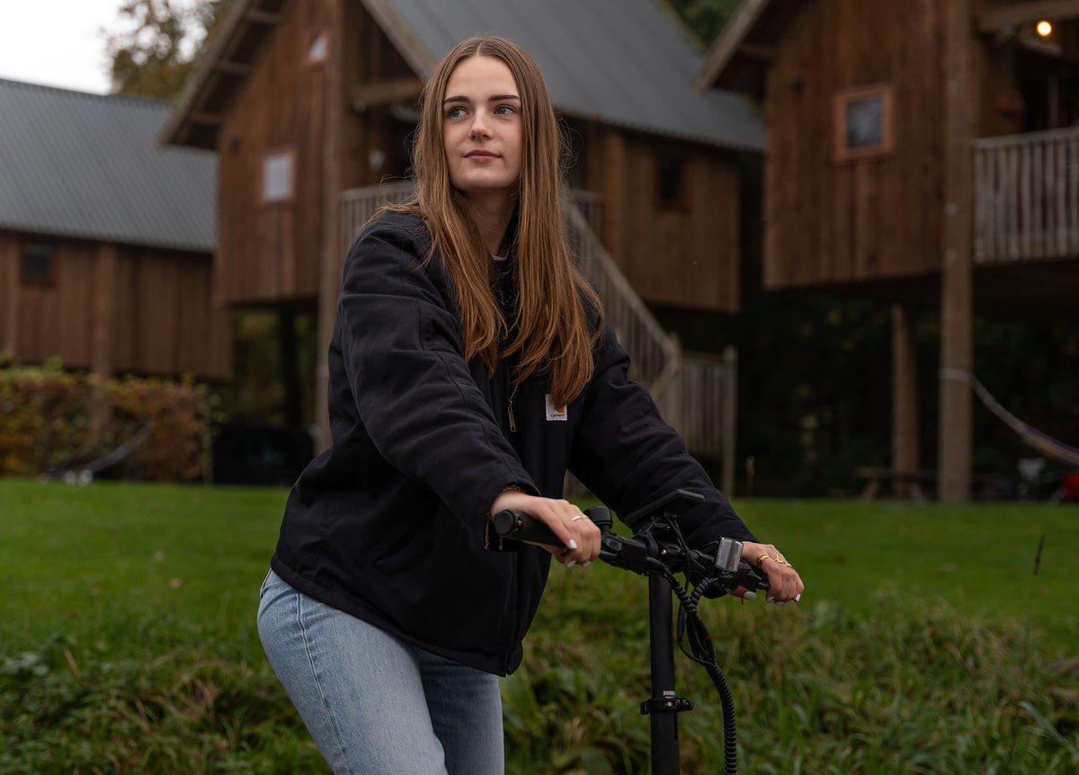 Image of a woman riding the Carbon Fibre 250 with wooden cabins in the background