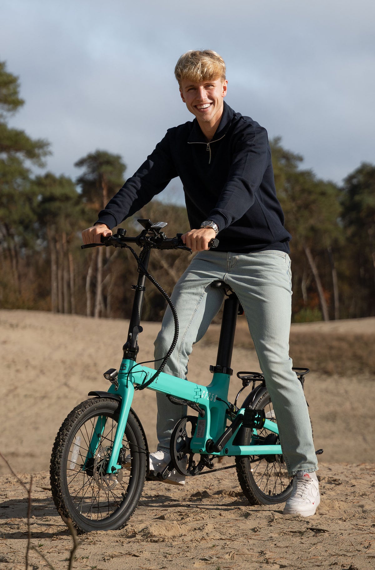 Lifestyle image of a man riding the Turquoise Carbon Fibre 250 folding E-Bike on a beach
